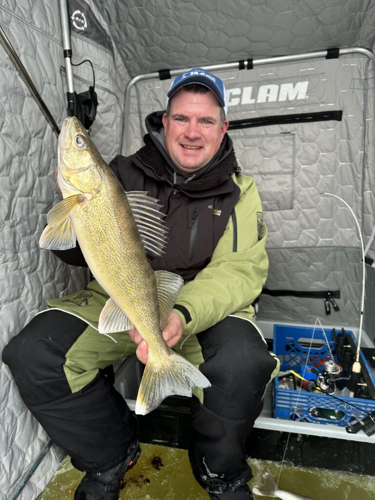 Angler inside ice tent holding a walleye during early ice.